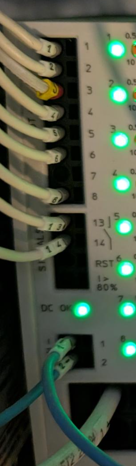 Close-up of a PLC/industrial controller: numbered terminal block with wires and lit green status LEDs along the side.